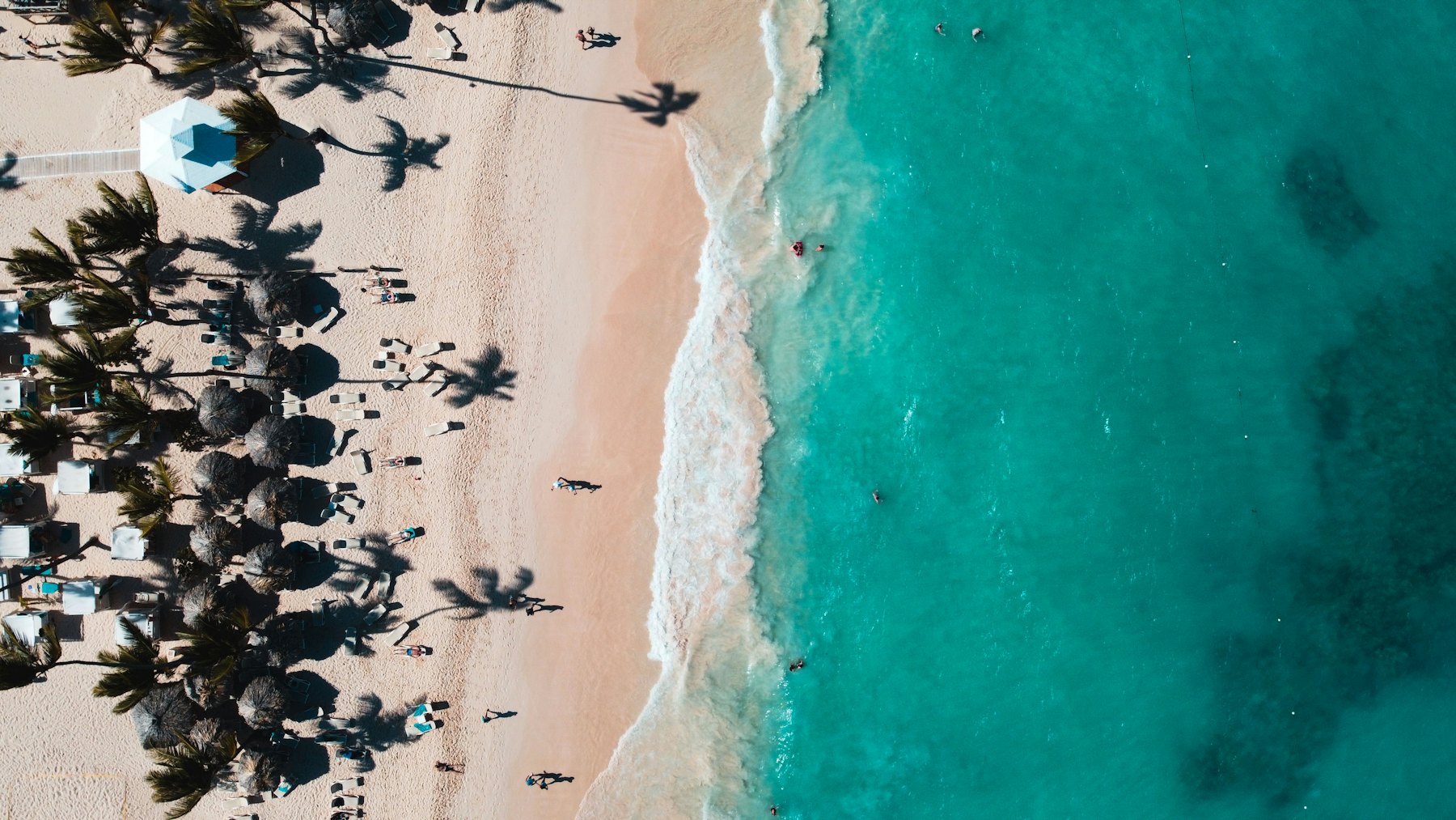 Vista aérea de gente en la playa desde bastante altura. Sirve para explicar ancho de playa sin identificar el resort.